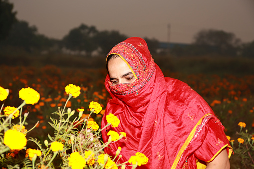 Beautiful, young woman of Indian ethnicity sitting among plants in bloom, enjoying the smell of flowers