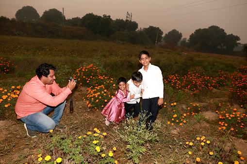 Father capturing photo of the children using Digital camera outdoor in the flower field.