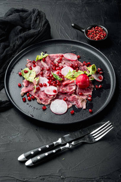 carpaccio di manzo, con ravanello e granato, su piatto, su fondo pietra nera - beef carpaccio foto e immagini stock