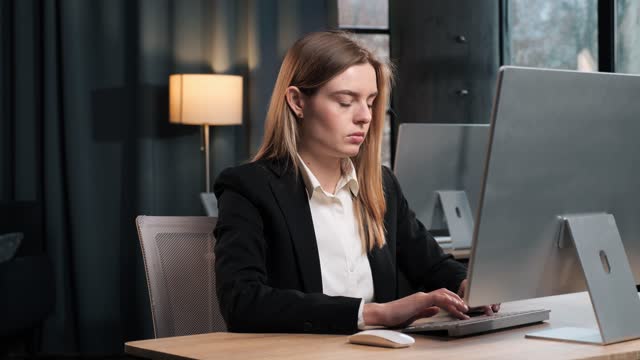 Young beauutiful focused female executive manager businesswoman in formal suit sitting at desk working typing on laptop computer in corporation office. Business woman working on pc messaging indoor.