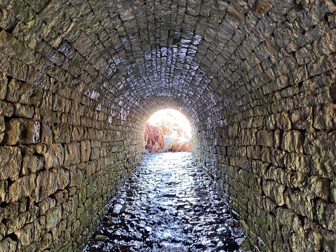 Old stone lined tunnel with a stream flowing through