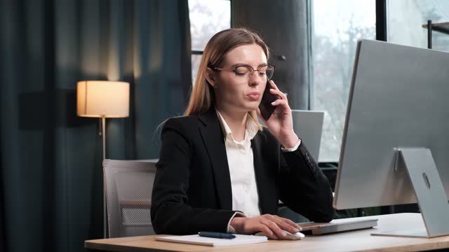 Smiling young business woman professional talking on phone using laptop sit at home office desk, happy female customer make mobile call confirming online website shopping order delivery concept.