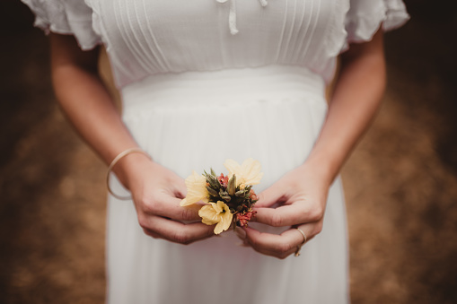 Pregnant mother in a white dress holding flowers in front of her belly outdoors