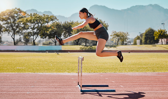 Jump hurdle, athlete and woman, for competition, on track and running to win, wellness and healthy. Fitness, female and girl training, exercise and workout for health, cardio and jumping for victory.