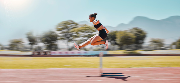 Athlete, sports and woman jump hurdle for track and field event for obstacle race or course for running, exercise and training for marathon. Female outdoor for sport, workout and energy at a stadium