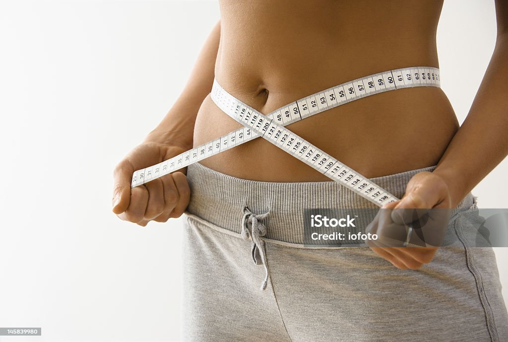 Woman showing she has lost inches off her waist Woman standing pulling measuring tape around waist. Body Mass Index Stock Photo