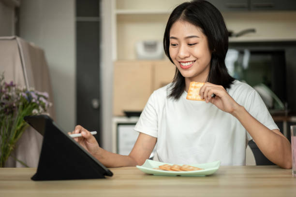 istock Woman is having breakfast with crackers mixed with various grains and using tablets to update her morning news, Small room in condominium background, Wake-up activities 1458400755