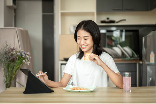 istock Woman is having breakfast with crackers mixed with various grains and using tablets to update her morning news, Small room in condominium background, Wake-up activities 1458400767