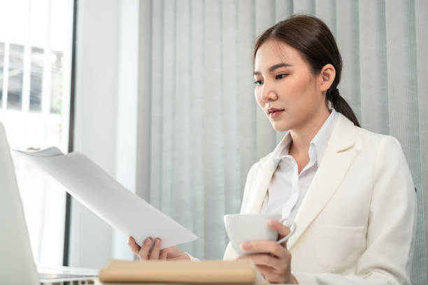 istock Professional businesswoman analyzing graph data from document in hand, Market research reports and income statistics, Woman working in a private office, Financial and Accounting concept 1458400841