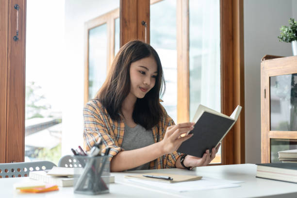 istock Young woman student reading textbook and doing homework assignment after using laptop to learning 1458400871