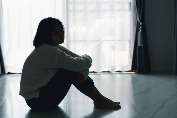 Concept of sad teenage girl depression. Upset teenage girl sitting at floor indoors. Anxiety young woman Despair and stress. Lonely and unhappy female are social victims. loneliness youth in home. stock photo