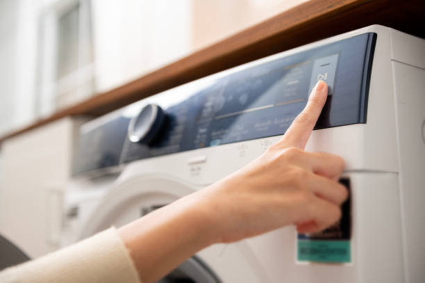 Close-up woman hand pushing washing machine buttons for setting program or start laundry  , health care lifestyle concept stock photo