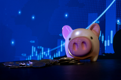 coins and piggy bank in front of the stock market screen