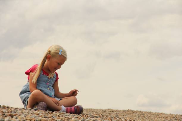 istock Little girl sitting on pebble beach 1458411482