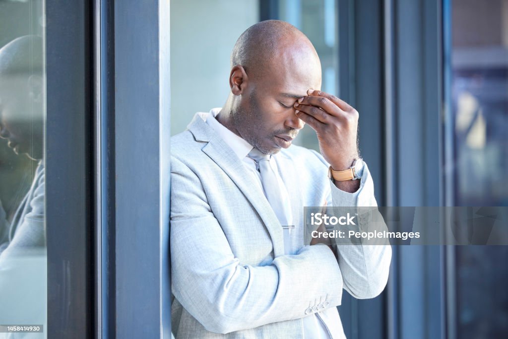 Stress, headache and tired African businessman outside the office taking a break from work. Frustrated, burnout and overworked professional manager working overtime at his workplace in the urban city Leadership Stock Photo