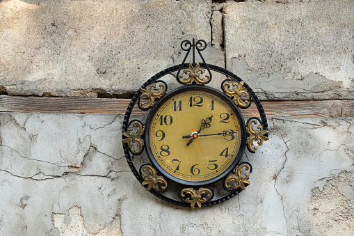 old broken clock ussr hangs on the white wall of a house in the street in the sun, broken old wall clock
