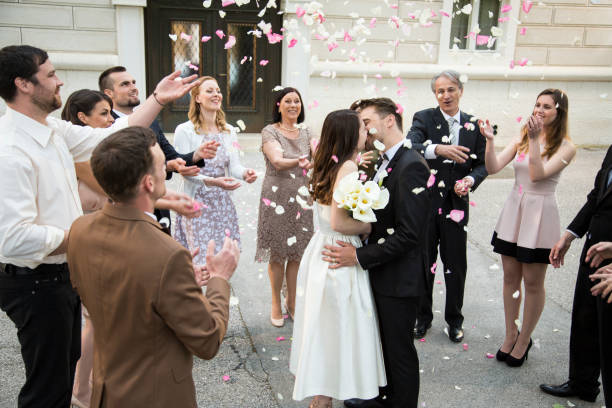 Guests throwing rose petals on bride and groom kissing stock photo