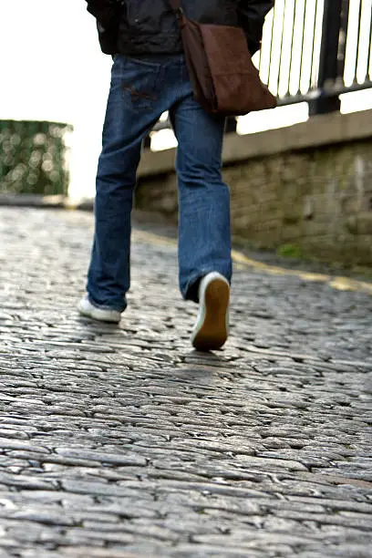 quirky shot of a man walking up a cobblestone street.