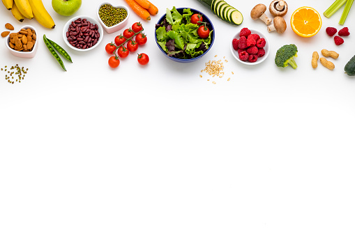 Top view of large group of healthy eating arranged side by side at the top of the image leaving a useful copy space at the lower side on white background. The composition includes a bowl of salad, fruits, vegetables, legumes, mushrooms and cereals.