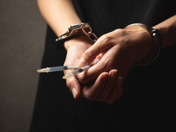 Handcuffs on wrist, drug syringe stock photo