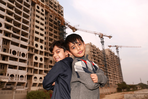 Two elementary student of Indian ethnicity standing near construction site back to back portrait close up.