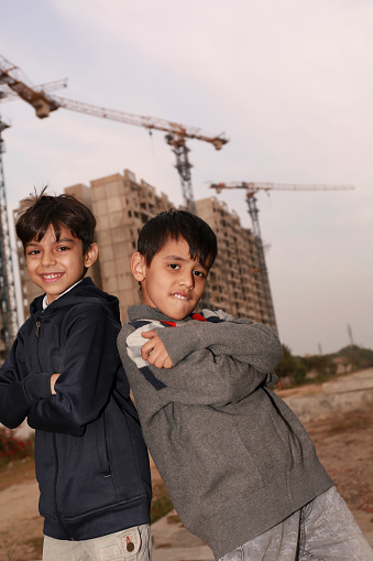 Two elementary student of Indian ethnicity standing near construction site back to back portrait close up.