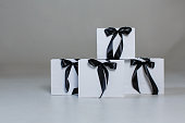 Four white paper gift bags with black bows on a gray background