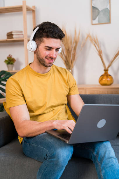 istock Cheerful man in headphones using laptop at home 1458446788
