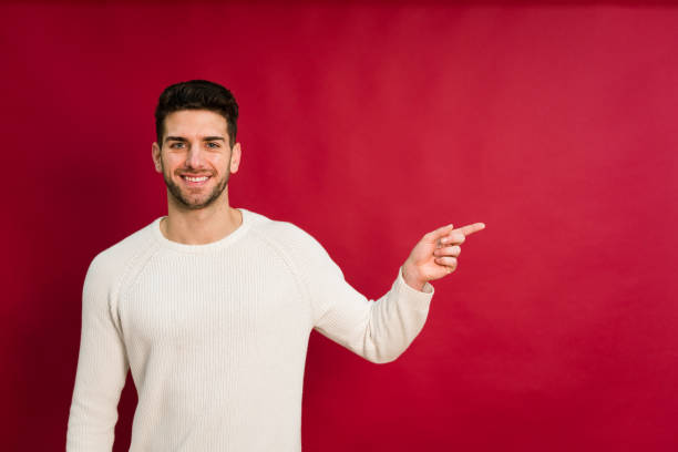 istock Cheerful young man pointing to the left on red background 1458450410