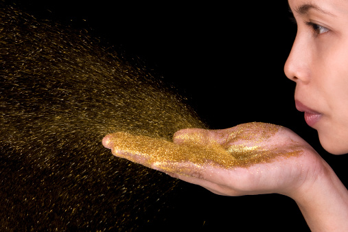 A young woman blow golden glitter from her hands.