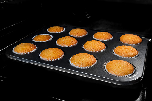 Twelve baked cupcakes, muffins in muffin tin in electric oven. Homemade bakery, food, cooking and pastry concept