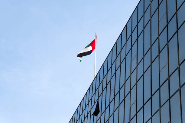 le drapeau des émirats arabes unis sur fond de ciel bleu. drapeau flottant au sommet du bâtiment moderne, symbole national des émirats arabes unis. concept de fête nationale et de jour du drapeau des émirats arabes unis. - flag of the united arab emirates photos et images de collection