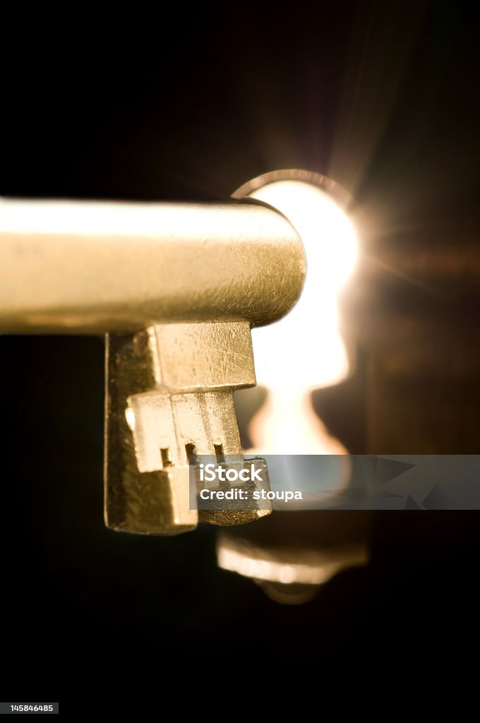 Key in a keyhole A golden key in a keyhole illuminated by a mysterious radiant light from the other side. Black Color Stock Photo