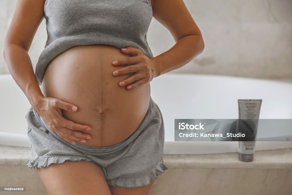 Unrecognizable Pregnant Indonesian Woman Applying a Stretch Mark Cream Close-up front view shot of unrecognizable pregnant Indonesian woman rubbing her big belly after applying a stretch mark cream Pregnant Stock Photo