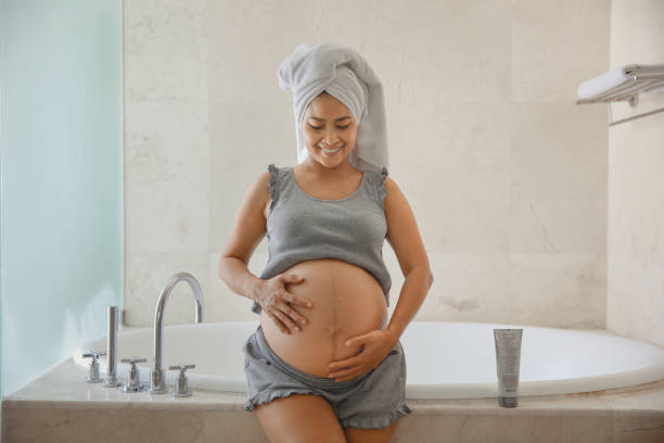 беременная индонезийская женщина, применяющая крем от растяжек - human pregnancy rubbing looking down abdomen стоковые фото и изображения
