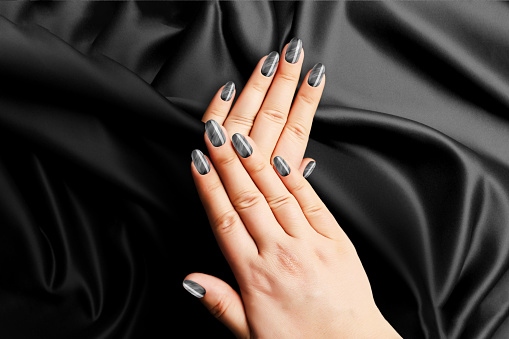 Black woman manicure on the dark fabric background. Seductive color. Two hands laying on top of each other.