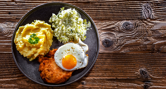 Breaded chicken cutlet served with fried chicken egg, potatoes and cabbage