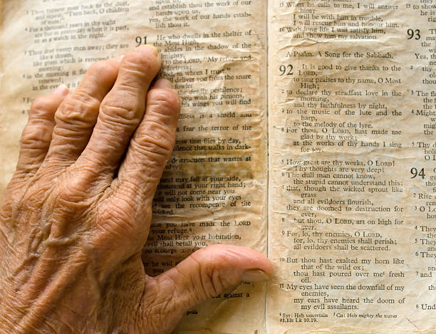 Hand on Bible Wrinkled, Arthritic hand of an old woman on an old, yellow, worn out bible turned to the page of Psalm 91. psalms stock pictures, royalty-free photos & images