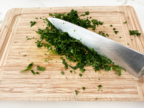 chopping parsley with kitchen knife on wooden cutting board