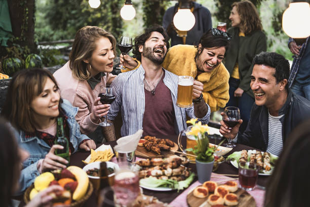 Multiracial group of hilarious friends have fun drinking beer and wine and eating together on the weekend at the restaurant table in the countryside Multiracial group of hilarious friends have fun drinking beer and wine and eating together on the weekend at the restaurant table in the countryside agritourism stock pictures, royalty-free photos & images