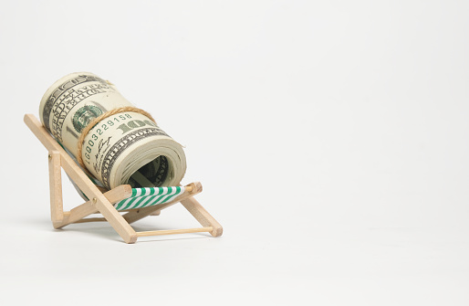 A picture of fake cash at the folding beach chair on copyspace white background. Retirement and vacation concept.