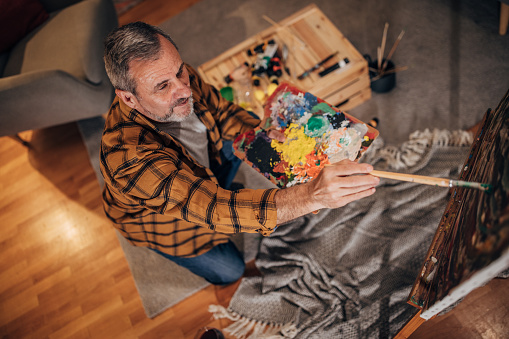 A man paints with a brush on a canvas in a studio