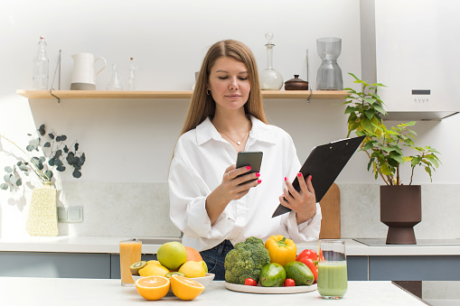 The nutritionist stands at the table with vegetables and fruits and makes a meal plan for the client. The concept of weight loss, healthy eating.