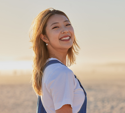 Happy, asian woman and portrait smile on the beach for fun, travel or vacation trip in the outdoors. Japanese female smiling for joyful holiday walk or traveling in happiness by the sandy ocean coast