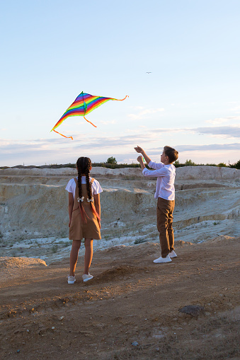 A boy and a girl fly a kite standing on the edge of a high cliff.