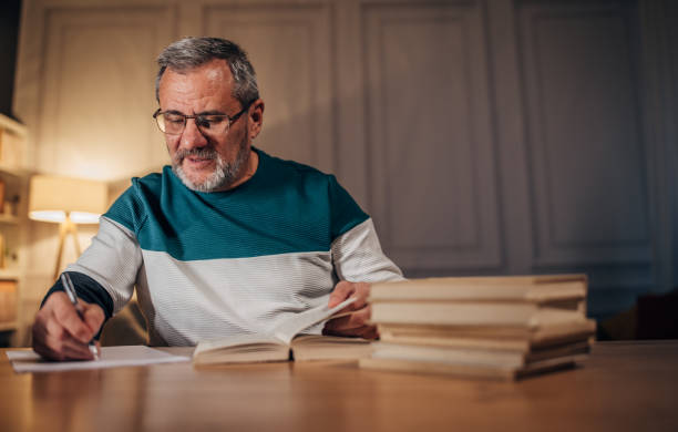 Small male figure in a suit reading a book while sitting on vibrant stacked books, creating a playful and creative scene.