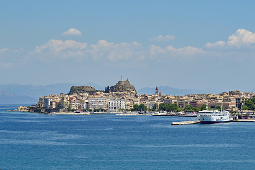 Corfu, Greece - June 2022: Waterfront of Corfu town with a ferry in the port and the old fortress in the background