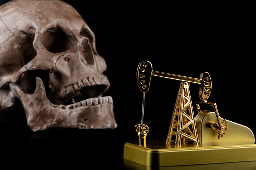 Golden oil pump and human skull on black background