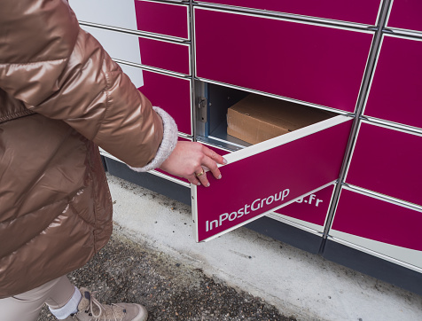 Loriol sur Drome, France - January 14, 2023: Picking up a parcel from a Mondial `Relay locker by a young woman. Lockers Mondial Relay. Pickup box a place by the road to send and receive parcels.