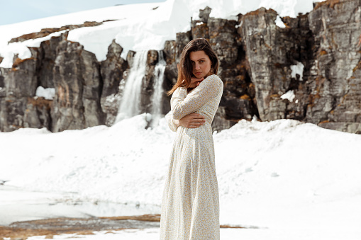 Woman in dress in winter snow landscape with waterfall in background